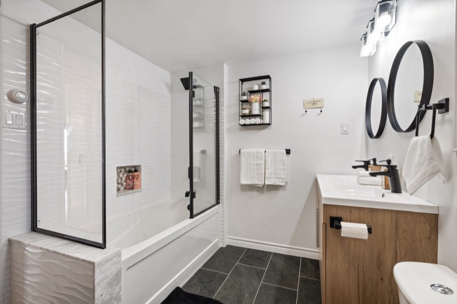 Main bathroom with tub and glass shower screen, wave tile and wood vanity